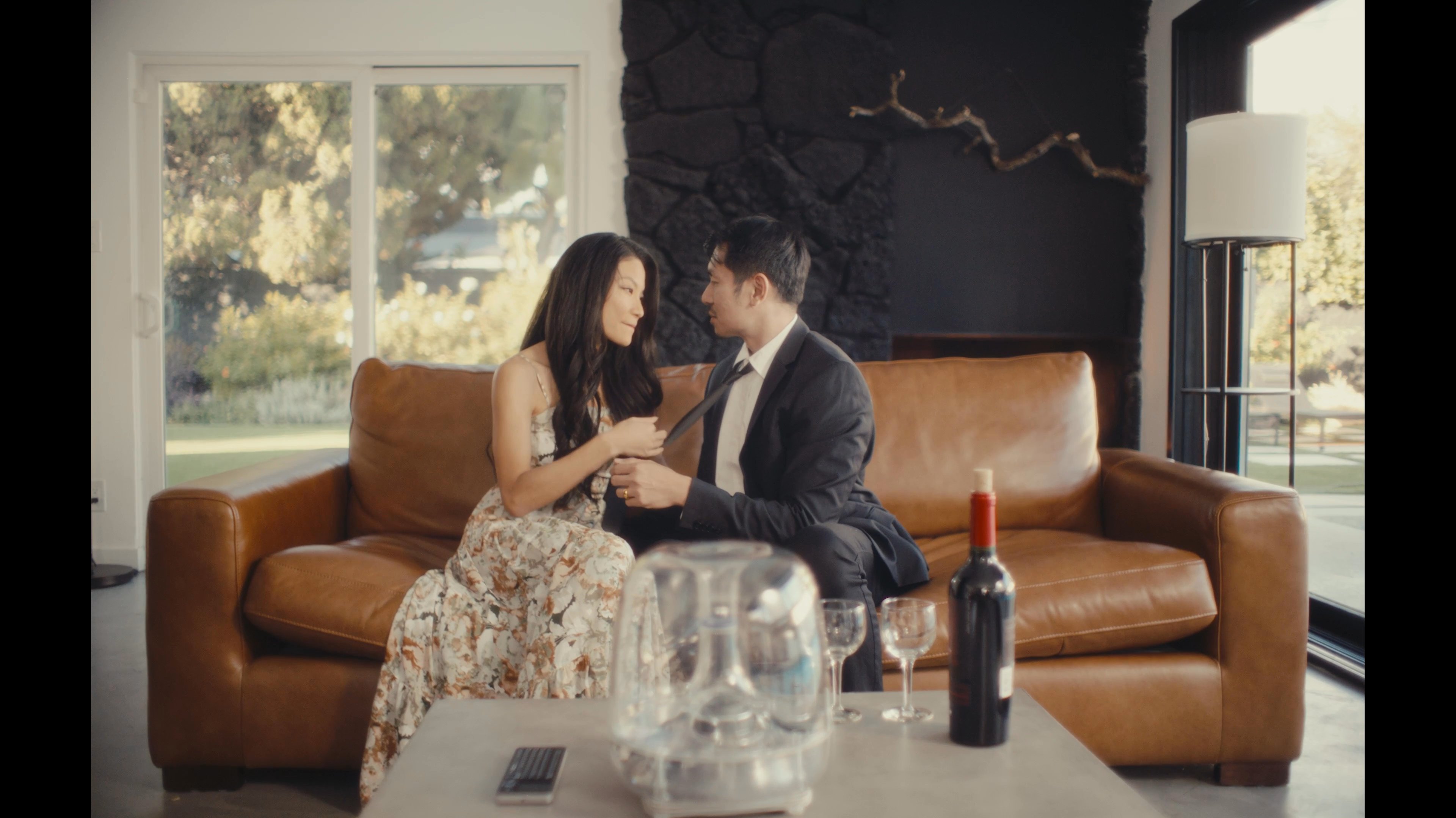 A well-dressed couple shares an intimate and romantic moment together while sitting on a leather sofa in a modern living room. The scene transitions to a focus on a high-tech, glowing orb-like device on the table, suggesting a blend of personal connection and modern luxury.