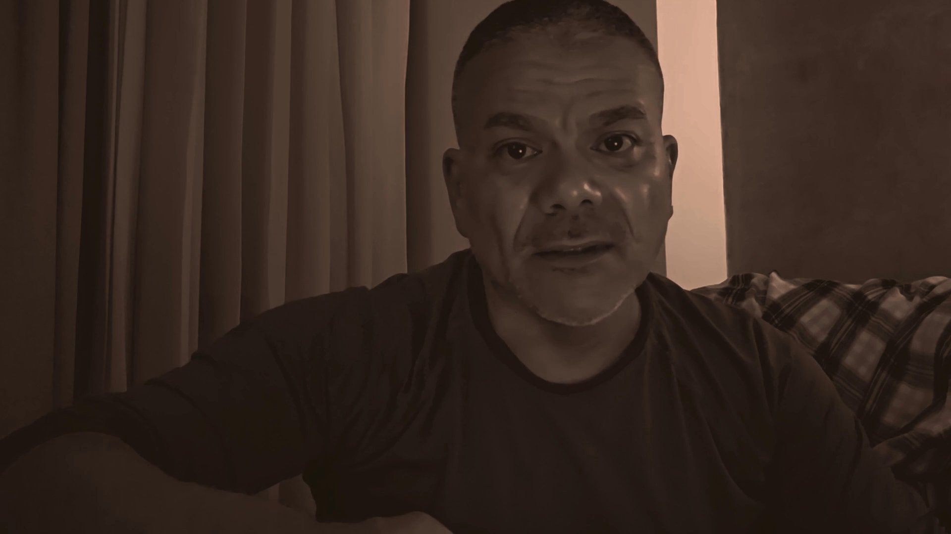 A man addresses the camera directly in a monotone environment, delivering a focused and expressive monologue to his audience.