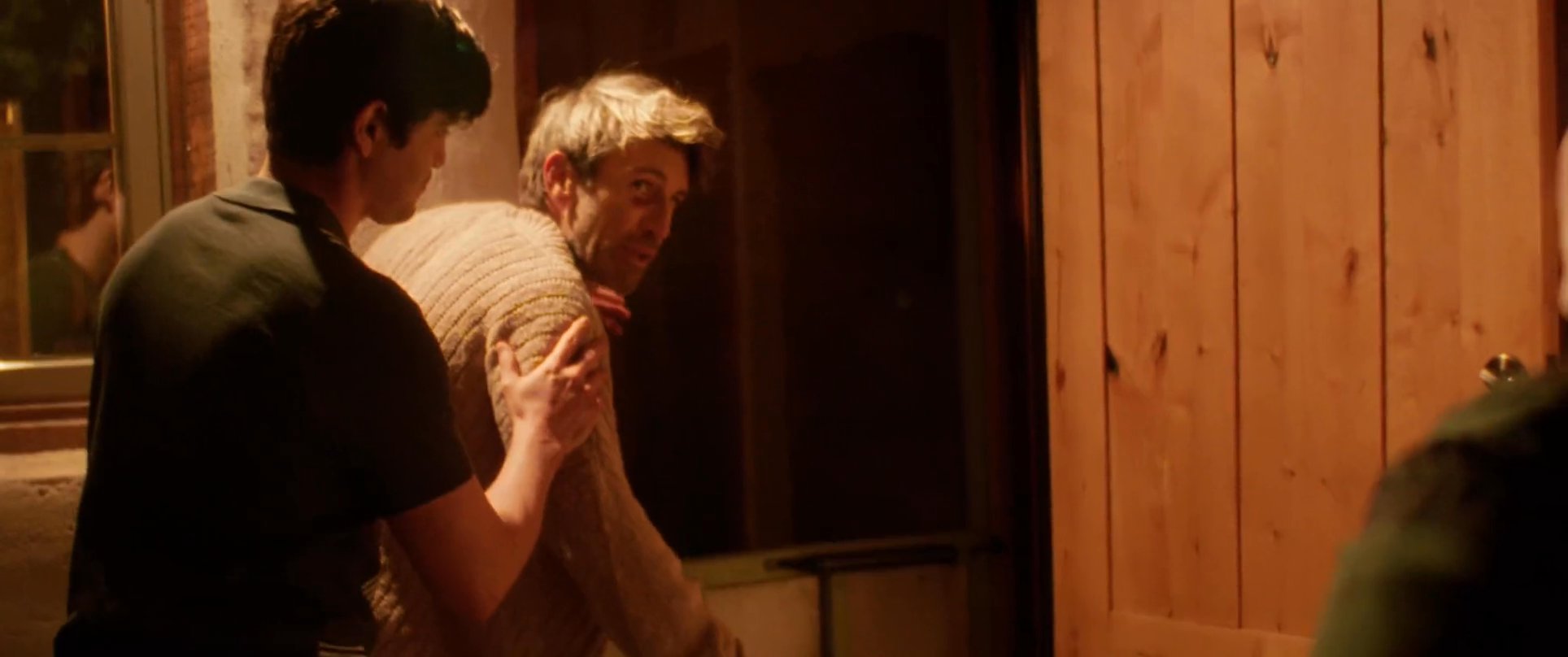 A group of individuals assists an injured man back to safety while tension unfolds between them in the dark of night. The scene captures the urgency of the medical situation followed by an emotionally charged exchange between the participants.