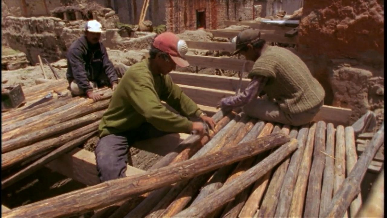 Craftsmen utilize traditional techniques and tools to restore the wooden roof structure of a historic Himalayan monastery. The work highlights the labor-intensive preservation of architectural heritage within a rugged mountain environment.