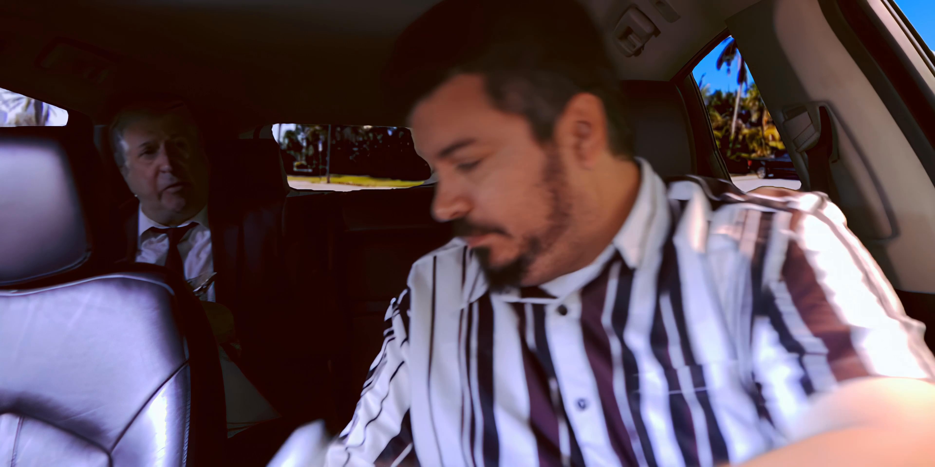 Two men in business attire engage in conversation while traveling in a vehicle, with one passenger eating a snack during the trip.