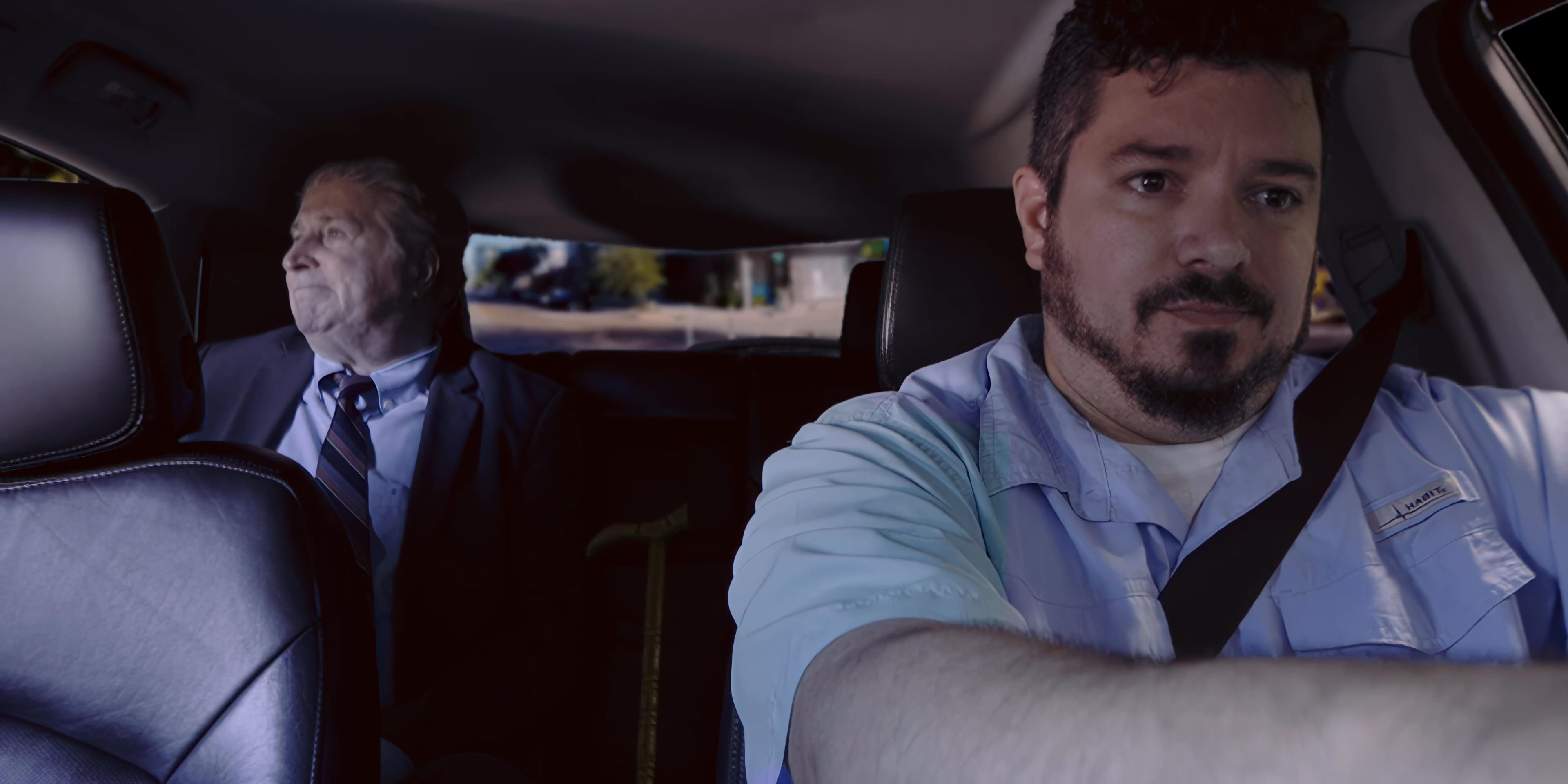An elderly passenger converses with a rideshare driver while being transported through an urban area.