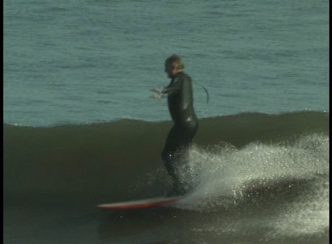 Surfers practice riding waves in the ocean while an instructor provides observation and guidance from the shore. The segment highlights technical surfing maneuvers and equipment preparation.