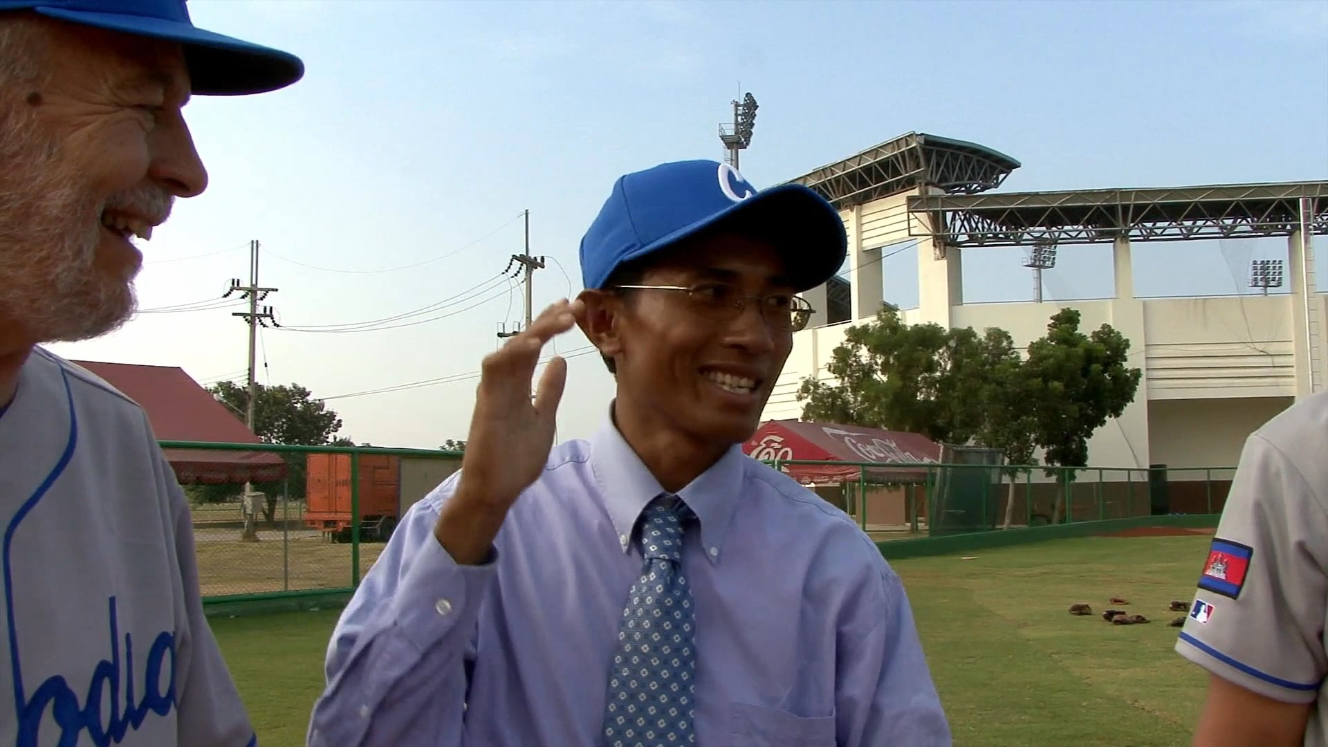 Coaches and players discuss strategy and training techniques on a baseball field in Cambodia. The team evaluates performance and tactical movements during an outdoor practice session.