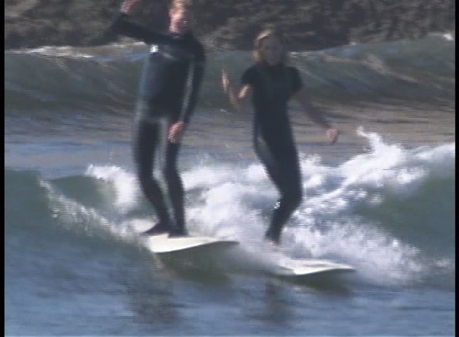 An experienced instructor provides guidance on surfing techniques while demonstrating maneuvers in the ocean. The clip features sequential shots of individuals practicing balancing and riding waves on longboards.