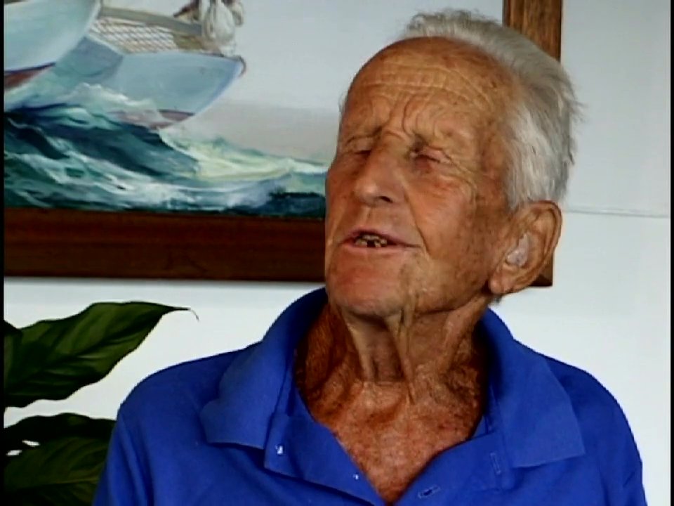 An elderly man shares his reflections while a woman skillfully crafts traditional floral leis, interspersed with scenes of rural island landscapes and surfing. These segments offer a cohesive look at Hawaiian historical practices and contemporary coastal life.