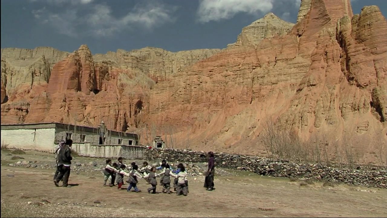 Children engage in outdoor play against a rugged, arid mountain landscape, contrasting with the Dalai Lama's insights on integrating traditional values with modern education.