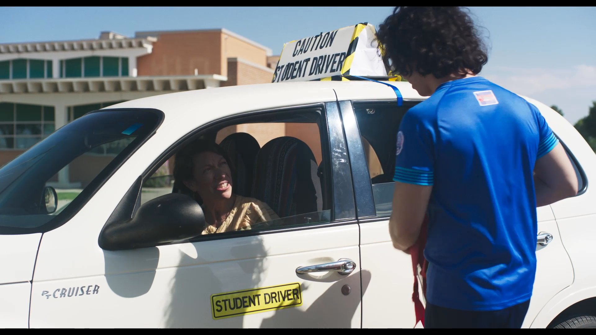A teenager communicates with a woman sitting in the driver's seat of a marked student driver vehicle. They engage in a supportive conversation during an outdoor driving lesson session.