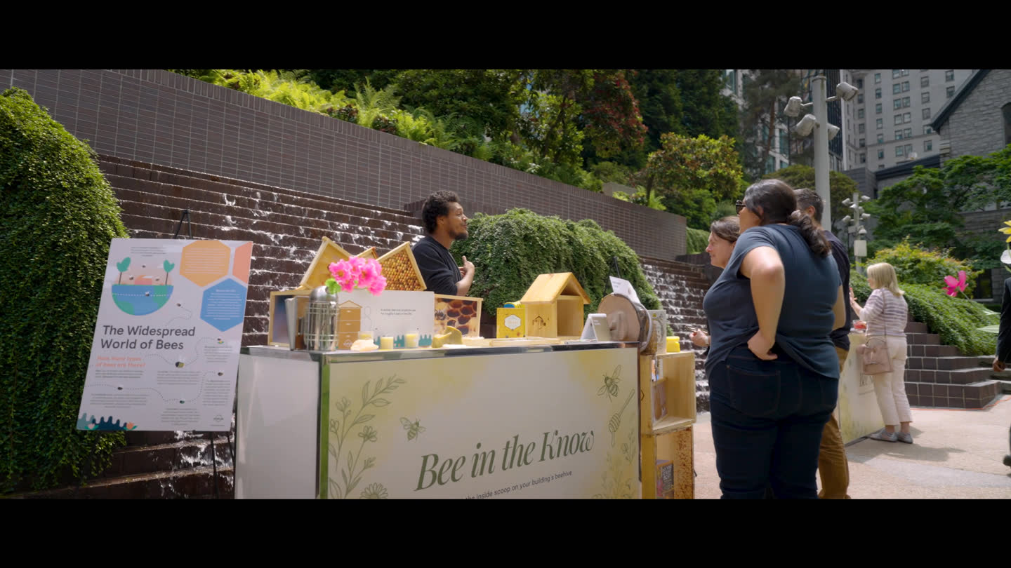 Film still: visitors speaking with an exhibitor at a community event booth