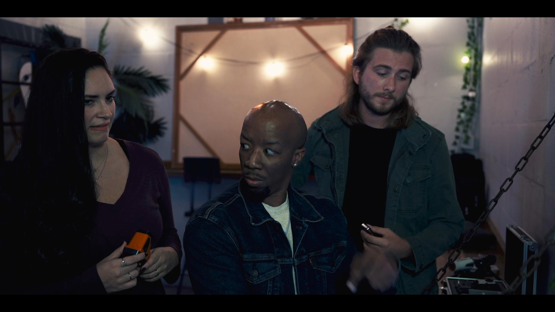 Three individuals collaborate in a dimly lit studio environment while engaging in a focused discussion regarding a project.