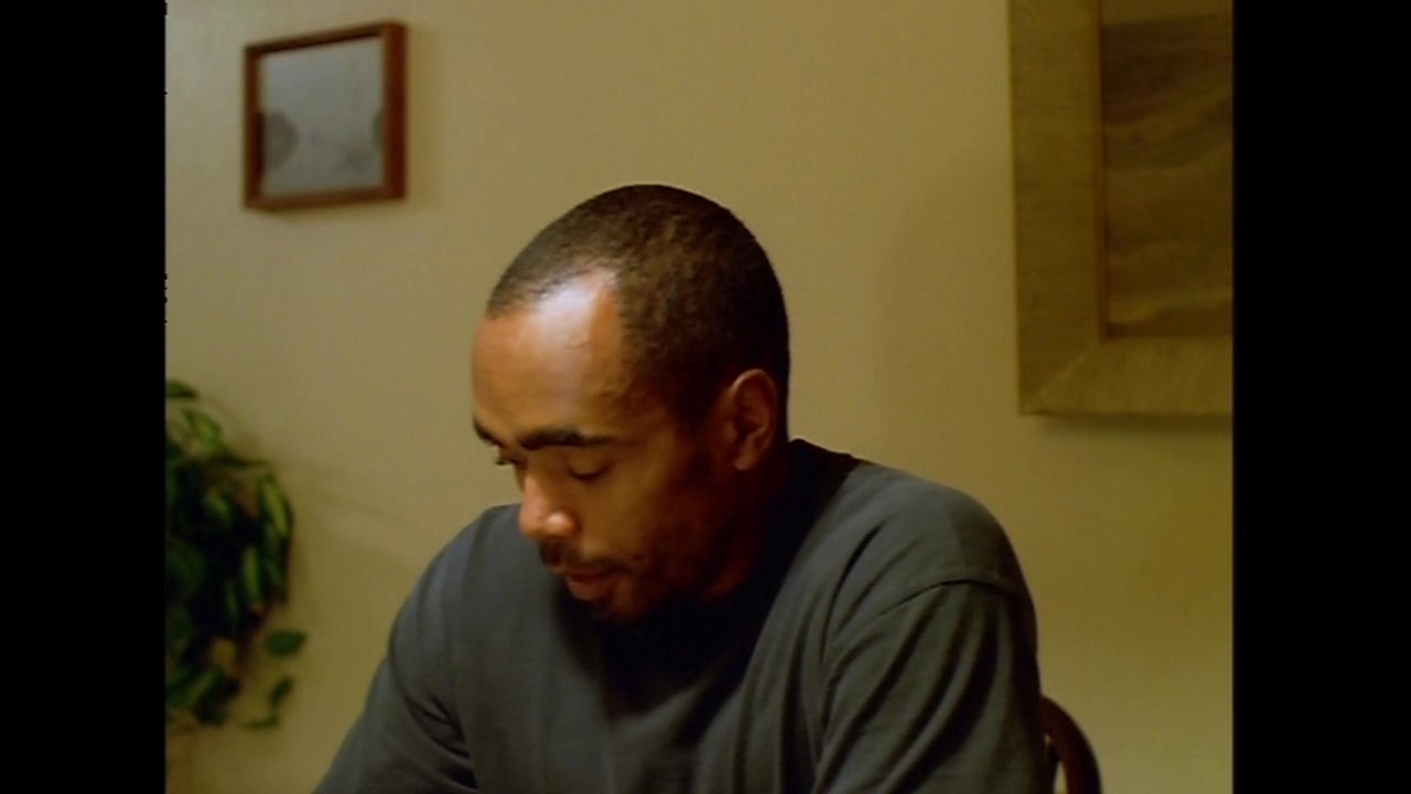 Friends share a meal at a dining table while engaged in conversation. The scene cuts between a man eating alone and two women sitting together at the table.
