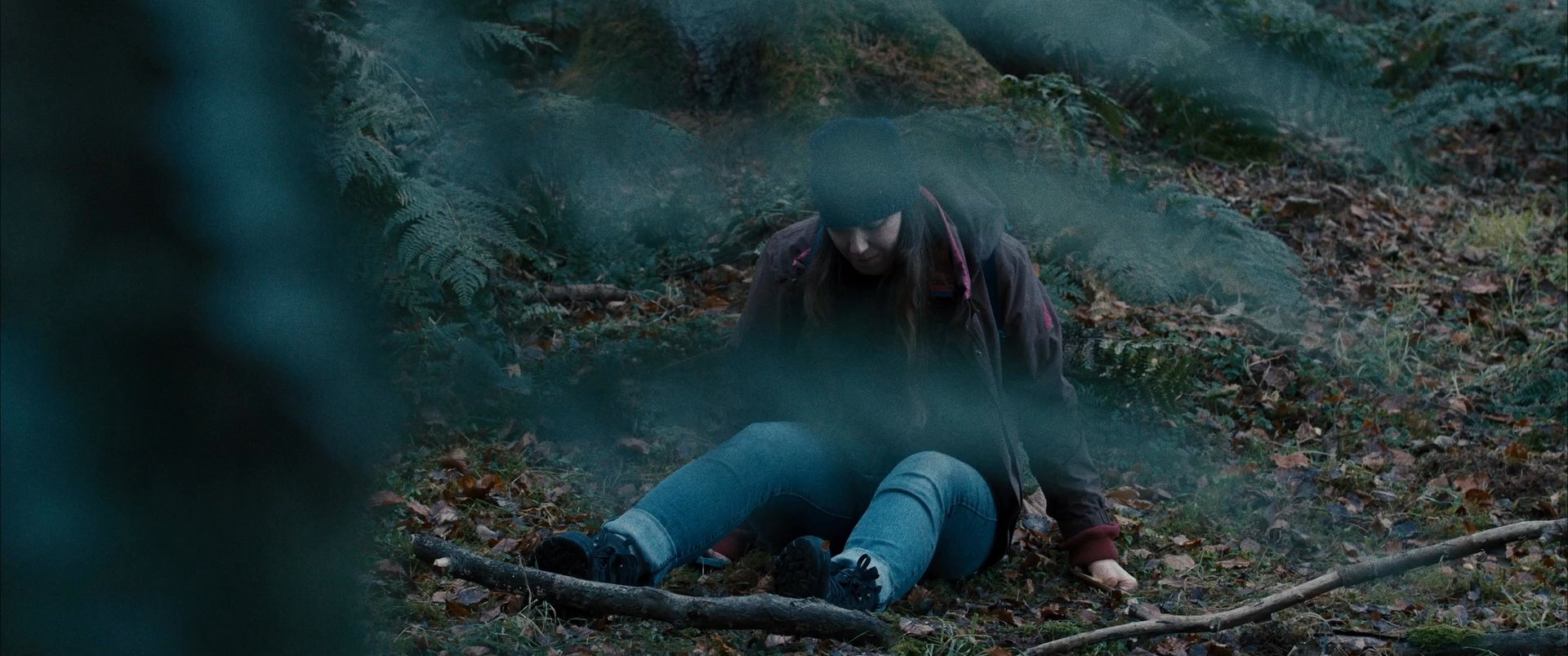 A woman sits on the forest floor checking her smartphone before gathering her belongings and continuing her walk through the woods. The scene captures the solitary nature of trekking through a dense, wooded environment.