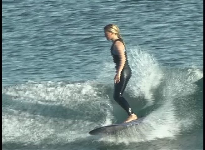 A surfer wearing a wetsuit maintains balance while riding a smooth wave on a longboard in the open ocean.