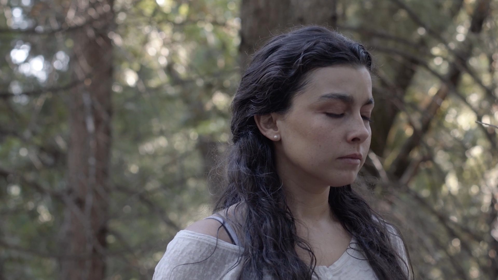 A woman stands in a dense forest, pausing to meditate and breathe before adjusting her belt in preparation for her trek.