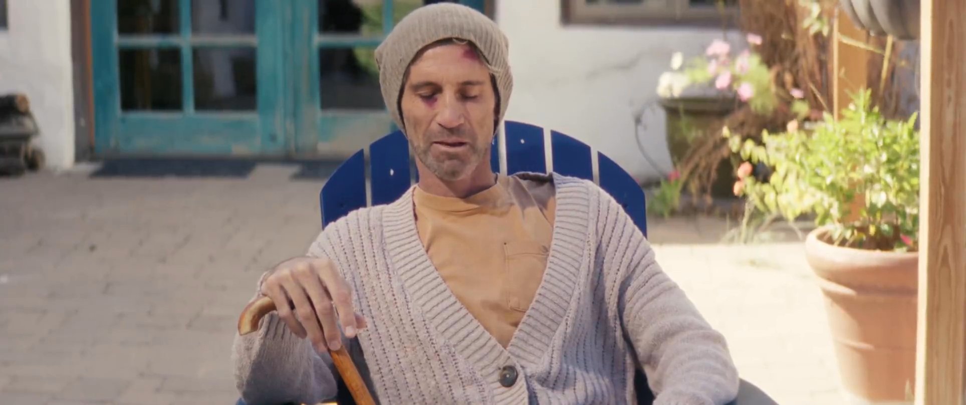 Two men engage in a contemplative conversation while sitting on a patio, interspersed with tranquil footage of flowing water. The interaction suggests a moment of personal reflection or supportive discussion.