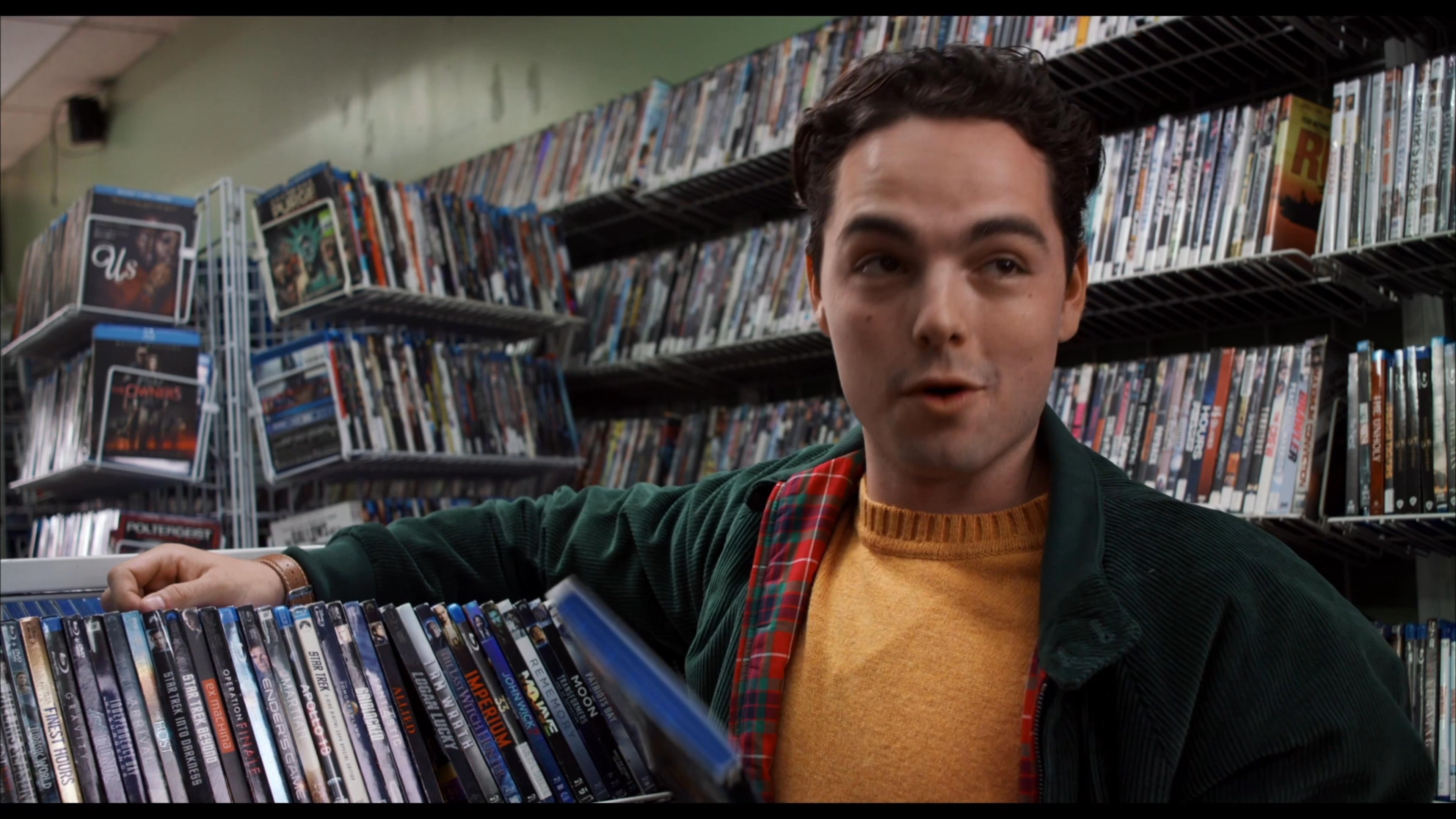 Two young men discuss movie selections while browsing shelves inside a neighborhood video rental store.