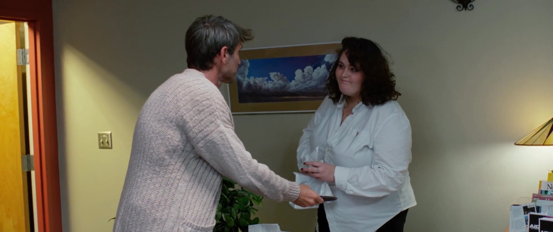 A man approaches a reception desk to hand documents to an employee, who receives and organizes the paperwork in a professional office setting.