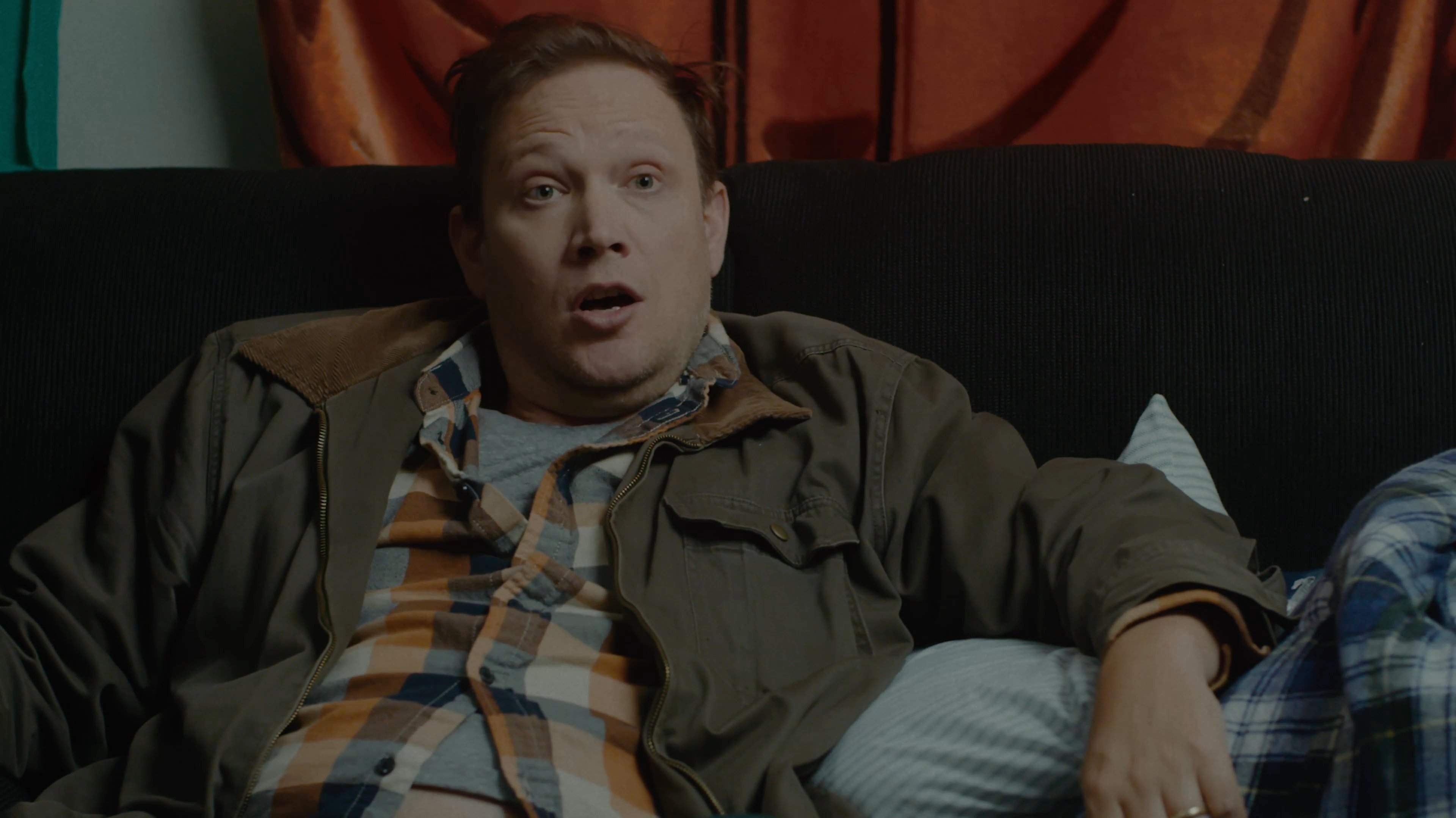 Two men engage in a serious, informal conversation while seated in a residential living space. They exchange viewpoints through active listening and expressive gestures.
