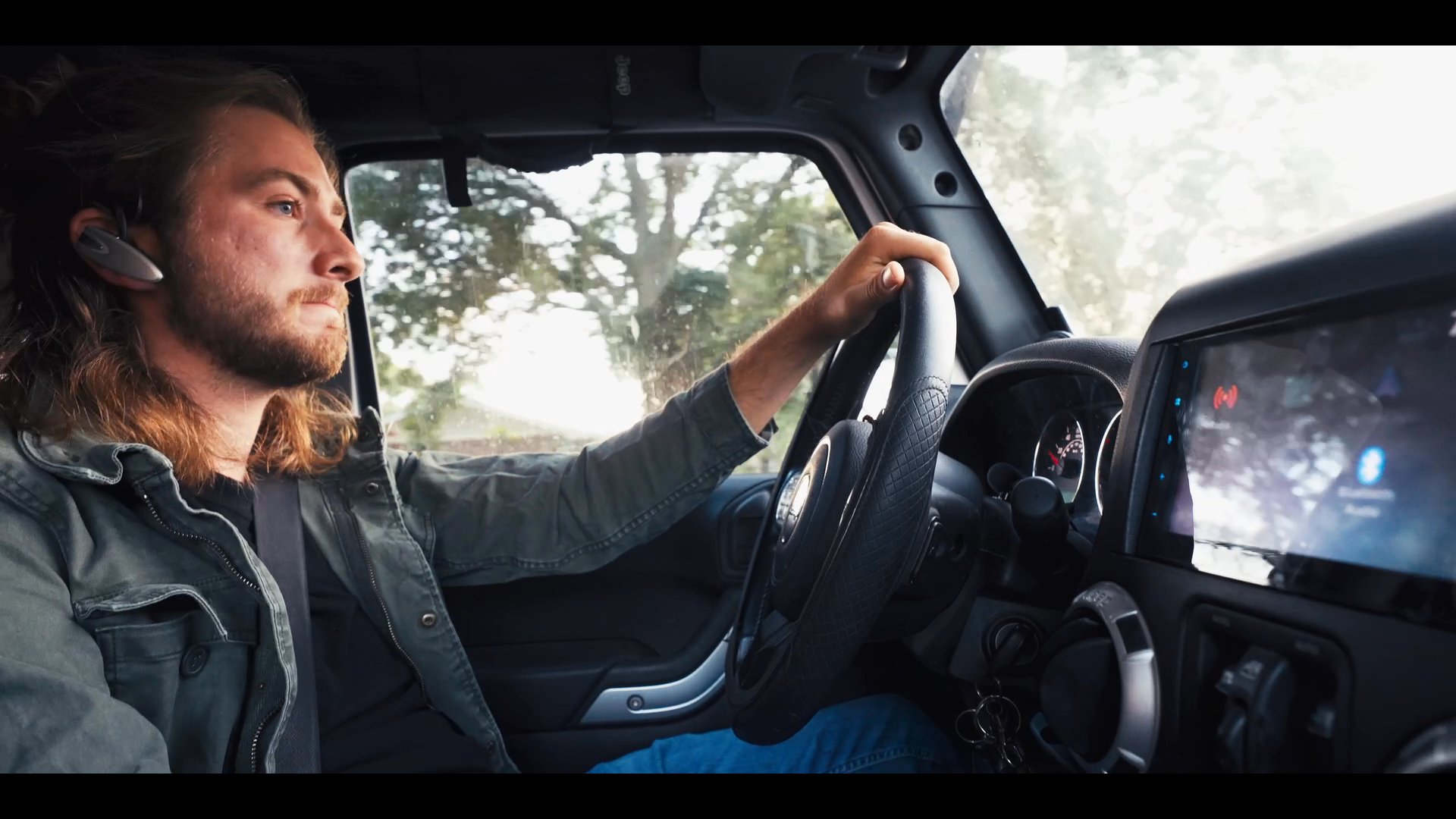 A man communicates via a hands-free headset while driving his vehicle, alternating with shots of another man speaking on a telephone in an outdoor setting. The sequence illustrates a connected dialogue between two individuals in separate environments.