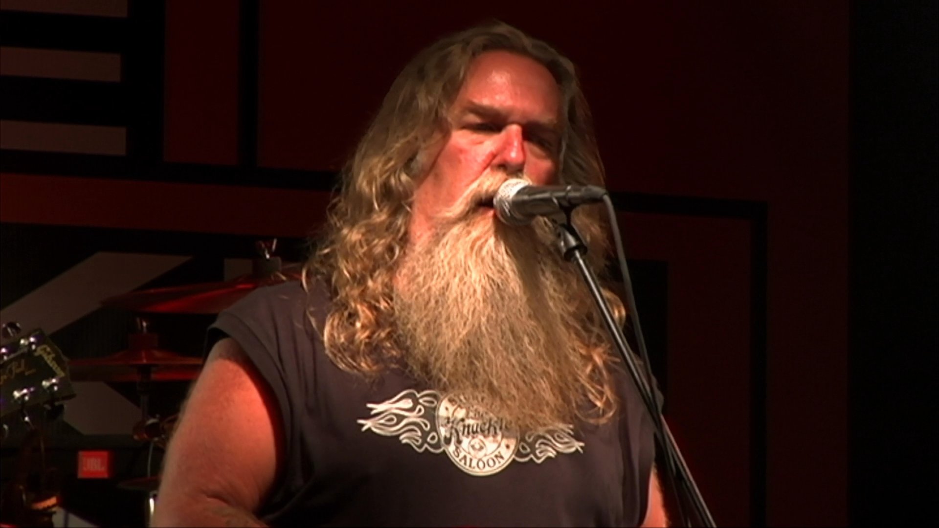 Patrons enjoy an evening of dancing at a crowded bar venue while a bearded musician performs live on stage.