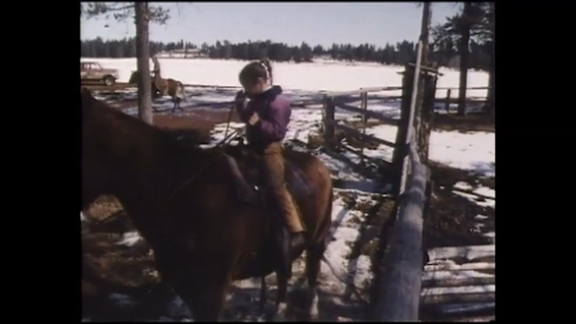 A young girl tends to a horse, then rides it through a fenced ranch enclosure amid patches of snow. The narration describes Nandi as a free spirit considering life as a rodeo clown, bullfighter, or buckaroo.