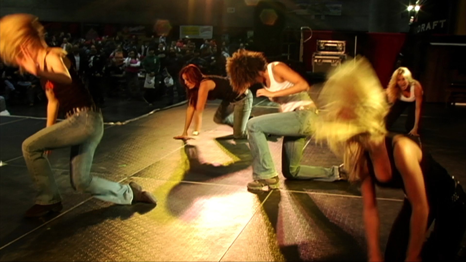 A group of female dancers performs an energetic, choreographed routine on a well-lit stage in front of an audience.