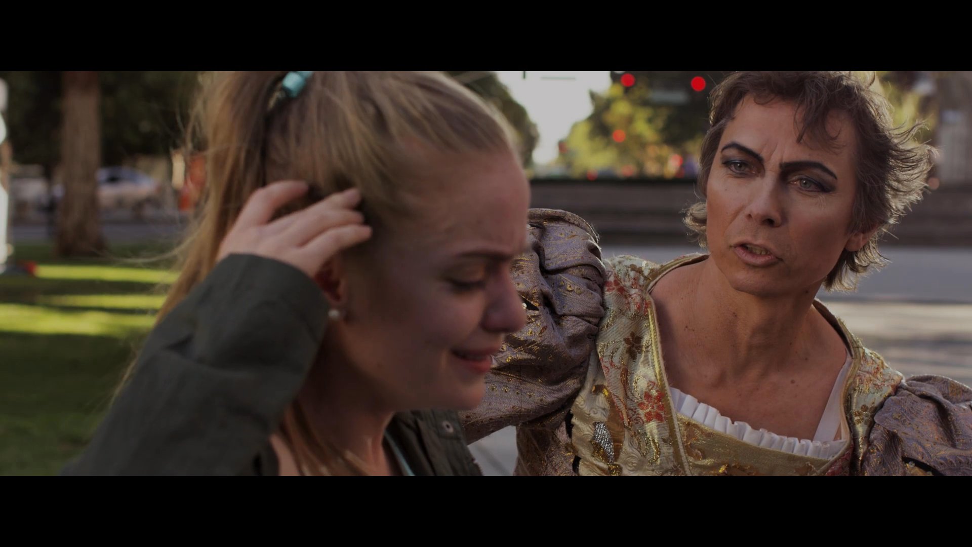 A distressed woman sits on a park bench, visibly upset while receiving comfort and advice from a costumed street performer.