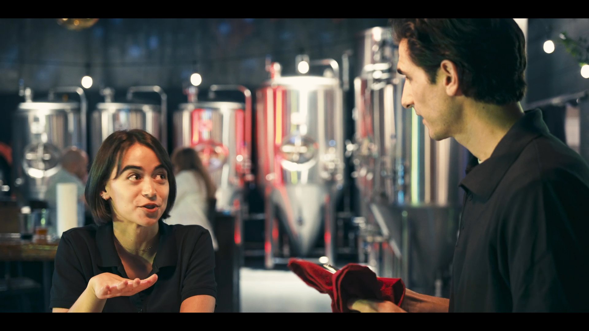 A staff member engages in a conversation with customers at a local brewery, while another pair of patrons plays a game of chess nearby.