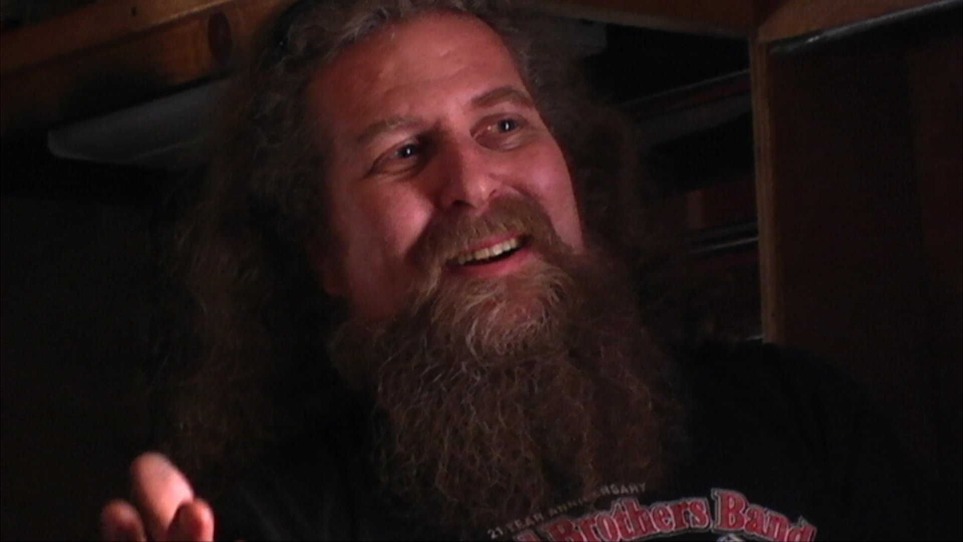 Musician Tommy Fryed of The Fryed Brothers Band shares personal experiences and insights during an intimate interview. The musician speaks candidly while seated in a dimly lit, wood-paneled space.