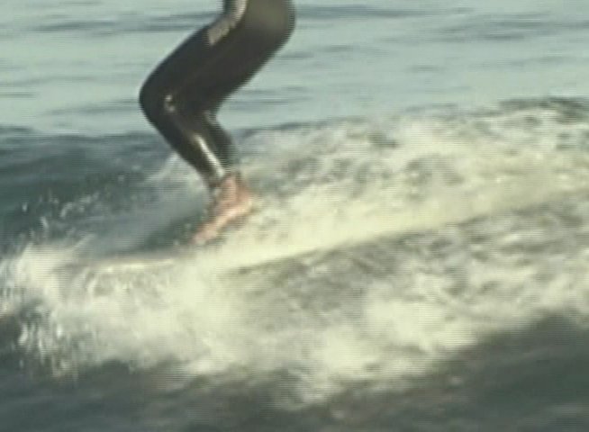 A surfer wearing a wetsuit skillfully maneuvers a longboard across the face of a breaking ocean wave.