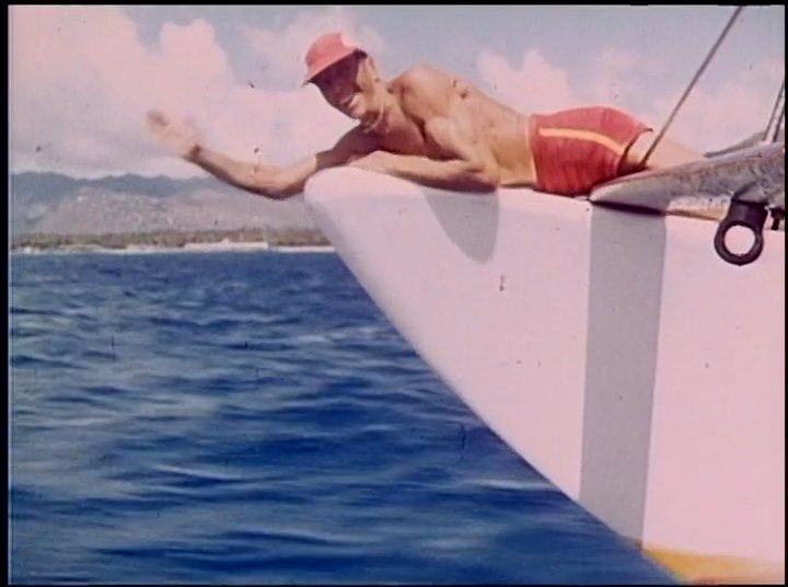 An elderly man recounts his experiences with sailing while archival footage illustrates him on a catamaran at sea, interspersed with shots of a scale model boat and shipyard construction.