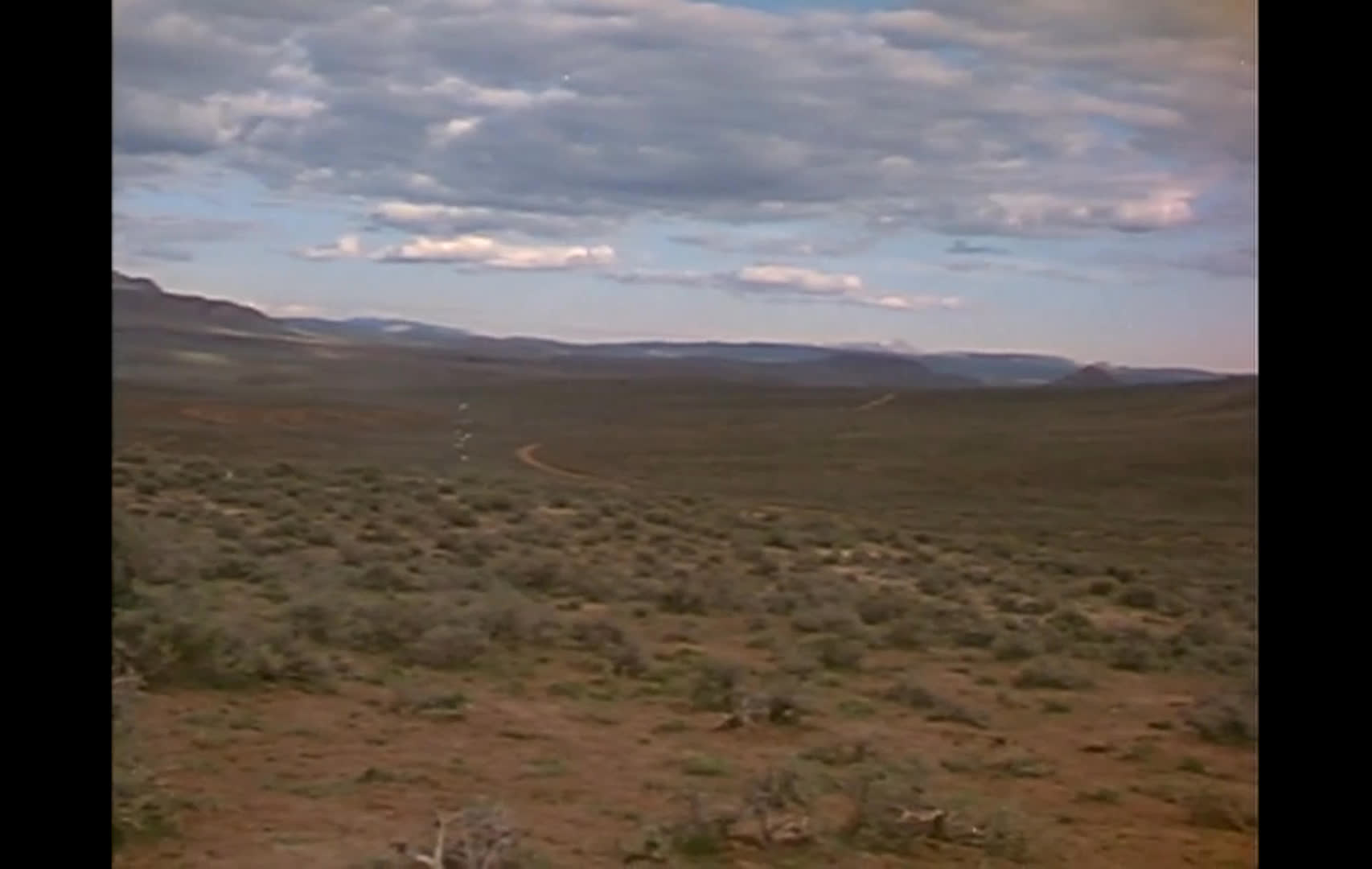 A horseback rider crosses a broad sagebrush range, followed by sweeping views of the open landscape. Bureau of Land Management representative Lee Delaney discusses competing interests in the use of range lands during an office interview.