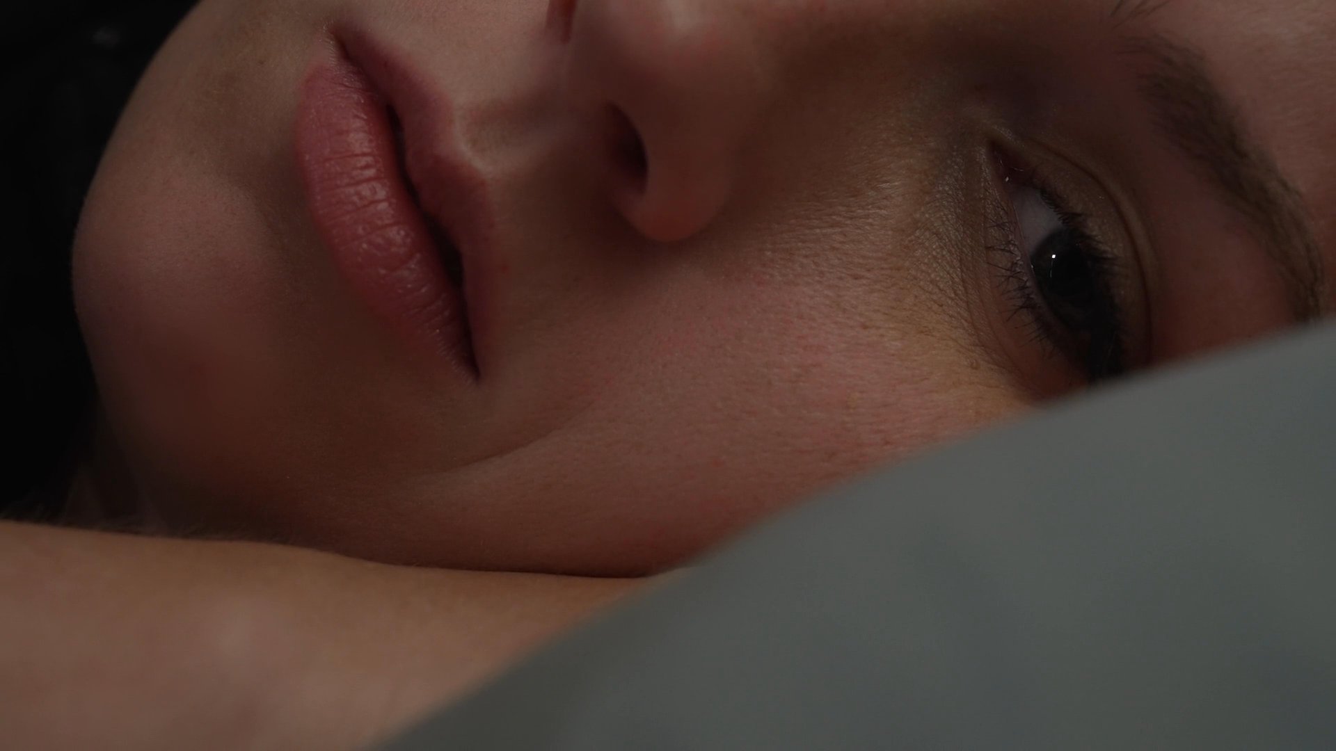 A transition occurs from a lively social gathering at a dinner table to a quiet, contemplative moment as a woman rests alone in a darkened bedroom. The sequence captures the contrast between communal engagement and individual solitude.