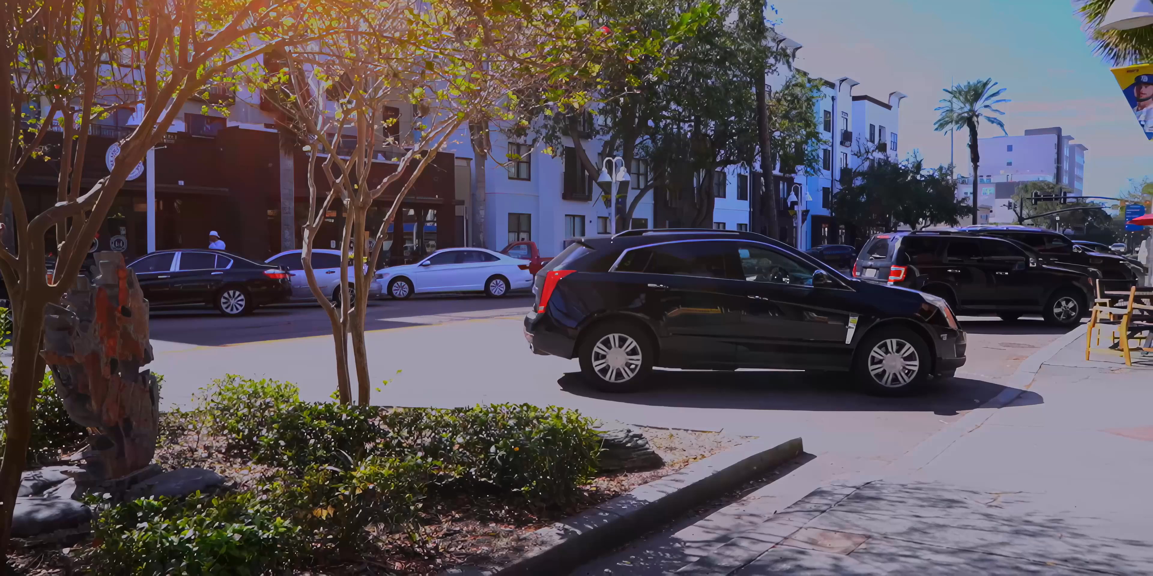 A black car navigates through a suburban commercial district before transitioning to a perspective from within the vehicle, featuring two men conversing during their transit.
