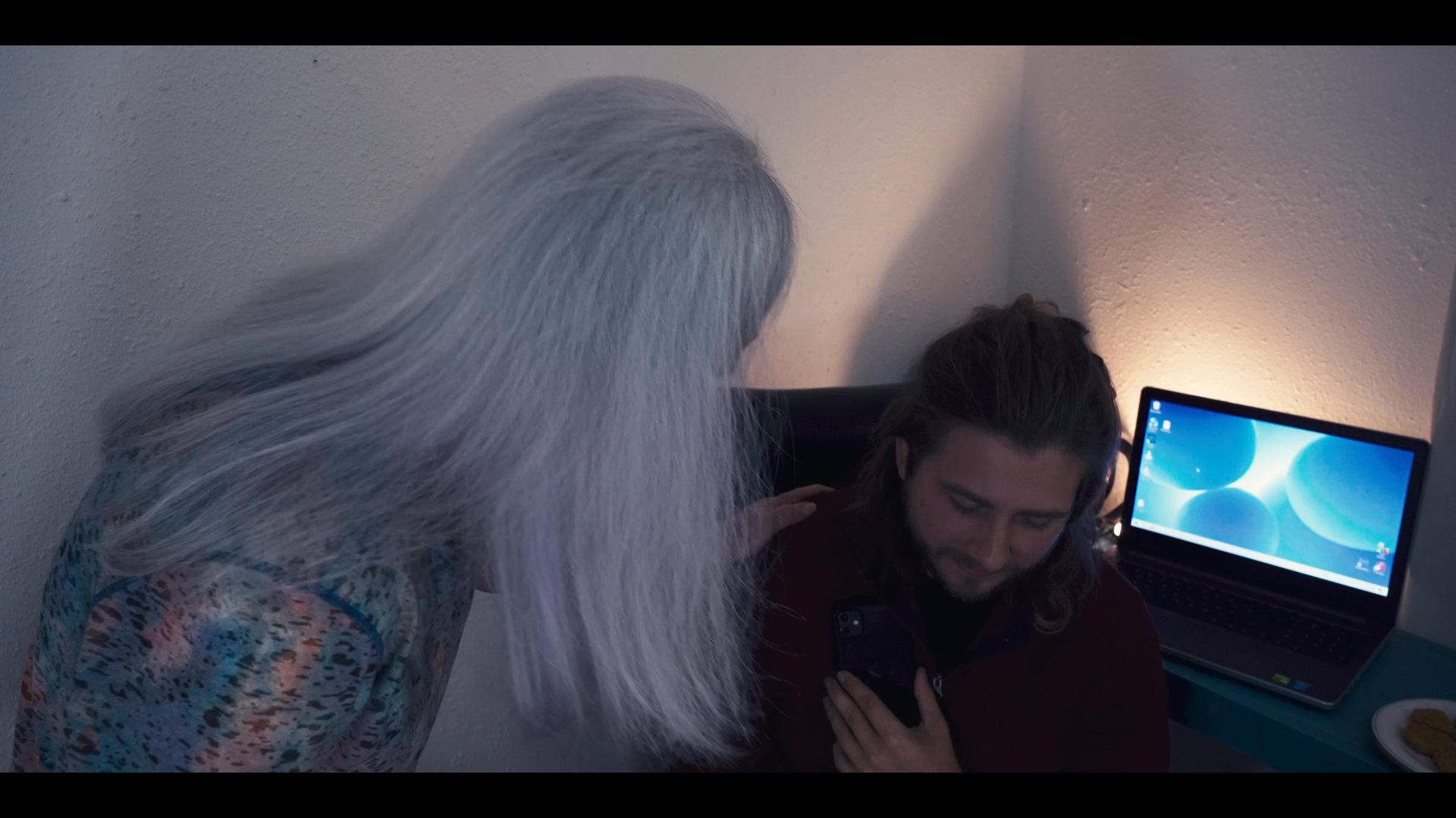 A woman provides emotional comfort and reassurance to a man while they engage in a serious conversation at a desk. The interaction involves physical touch and attentive listening to address the man's distress.