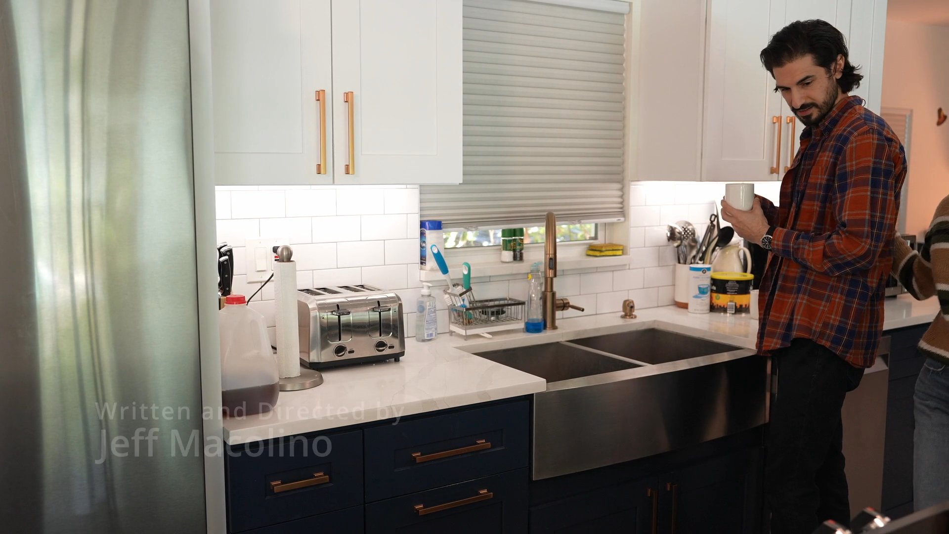 A man and a woman share a morning routine in a residential kitchen, interacting while preparing coffee. The scene highlights casual domestic cooperation and conversation.