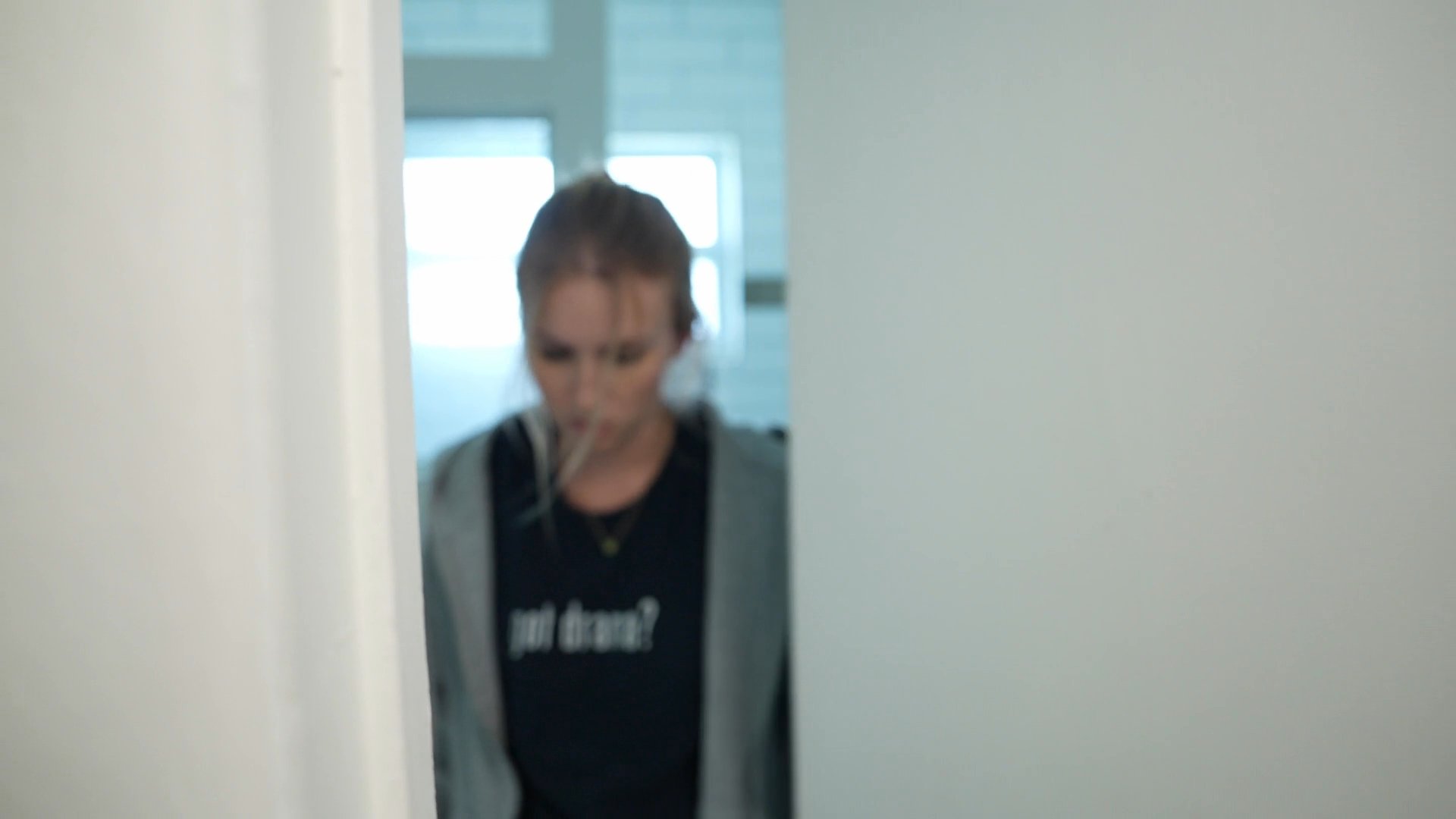 An older man and a young woman engage in a tense, silent exchange across a bathroom threshold, characterized by frustrated facial expressions and abrupt movements.