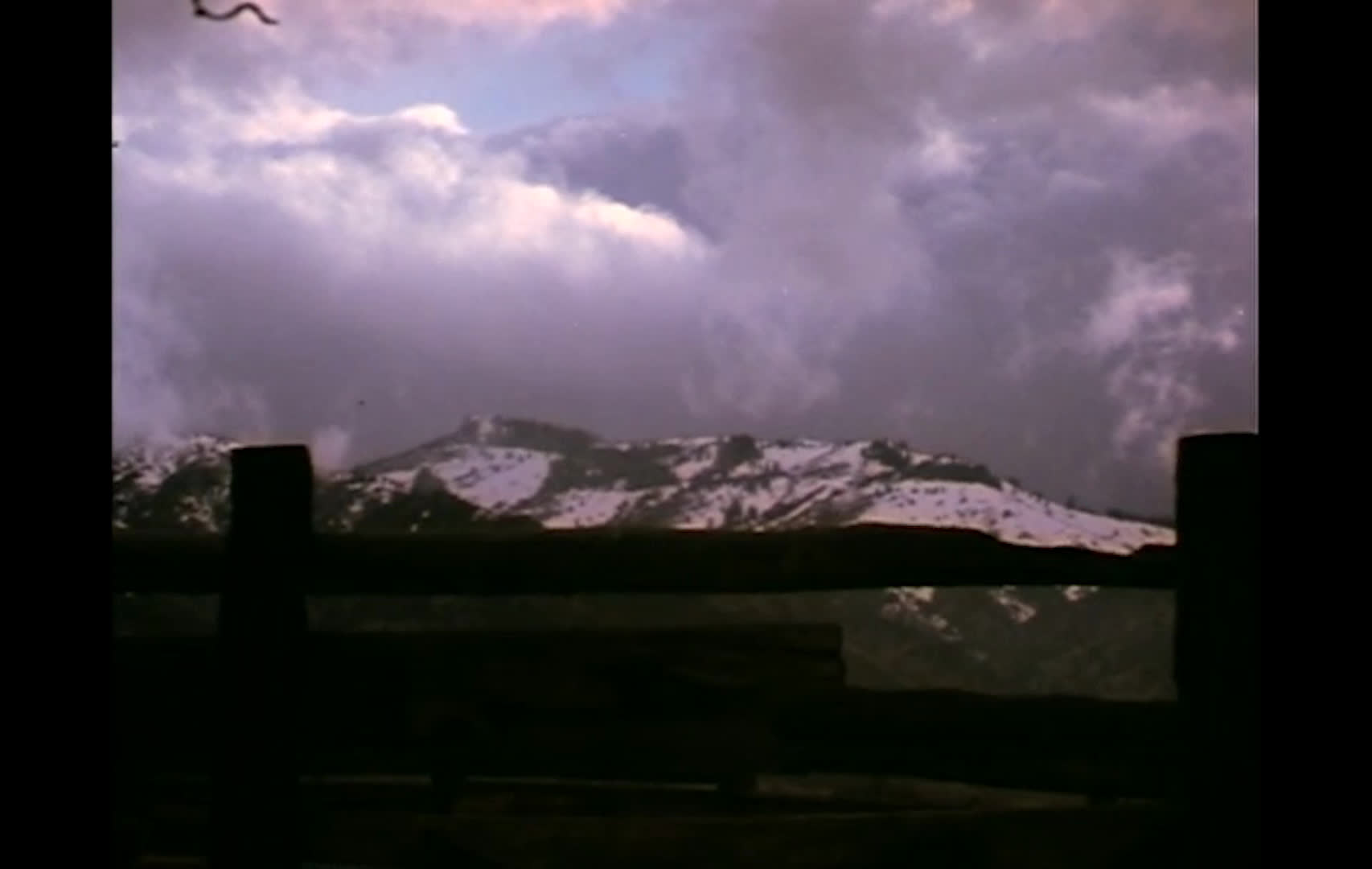 Cattle gather at a feed barrier as winter preparations center on having the herd and hay ready. Snow-covered mountains, a farmhouse chimney, and a snowbound valley convey the harsh conditions awaiting in December.