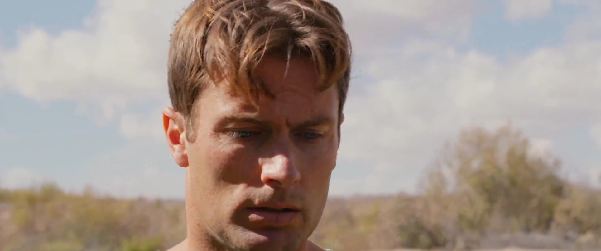 Two men engage in a serious and emotionally charged conversation in an outdoor, tree-lined environment. Their facial expressions convey rising tension and concern throughout the exchange.