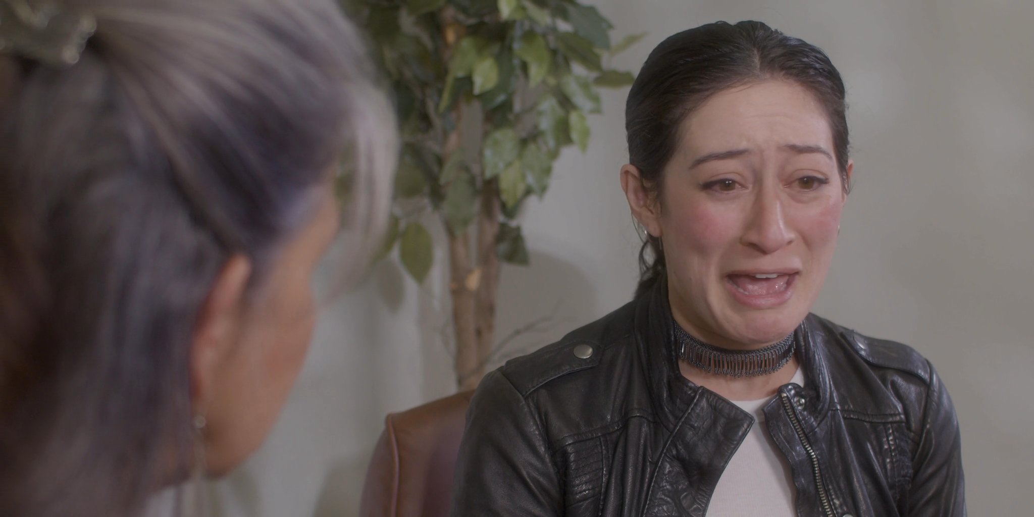 A woman expresses deep emotional distress while engaged in a vulnerable conversation with a female therapist. The session focuses on processing difficult feelings within a professional setting.
