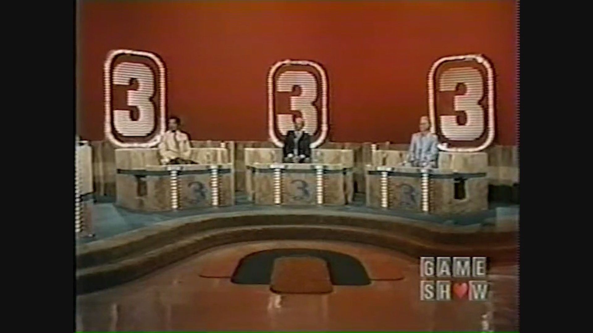Contestants seated on a television game show set engage in a competitive segment while a host moderates the proceedings.