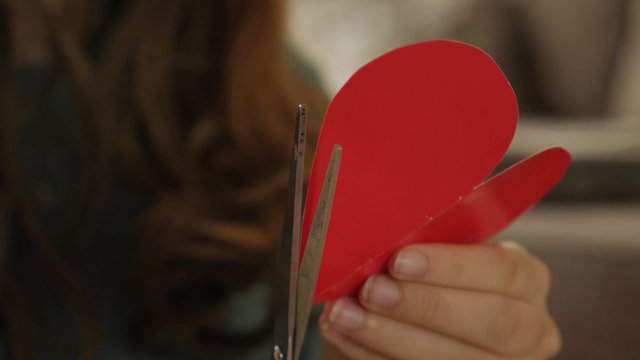 Girl cutting a red, paper heart with scissors