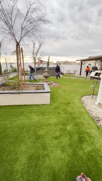 Artificial turf lawn with raised stucco planter beds, newly planted trees, and fountain