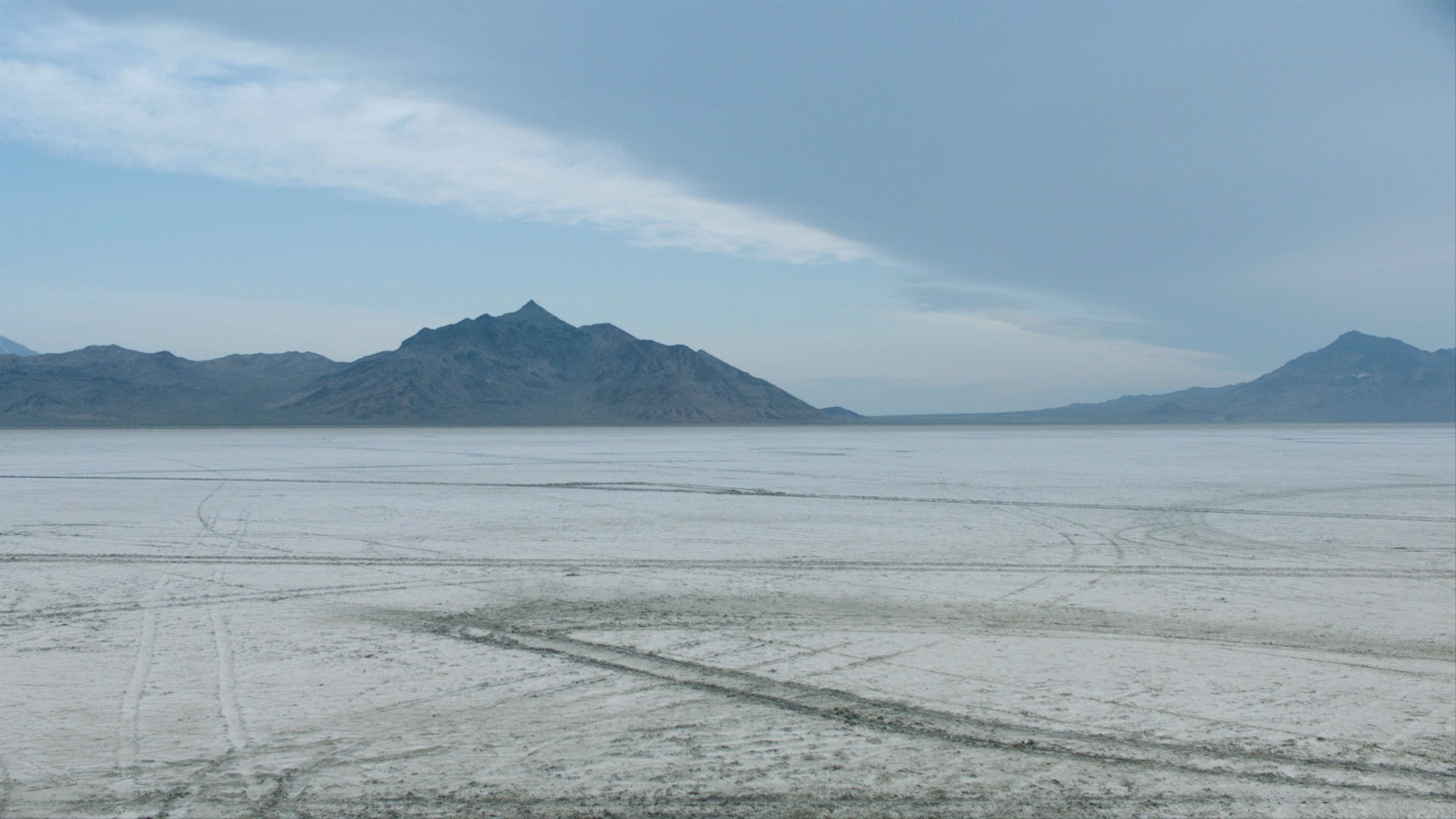 Land Rover driving across salt flats with mountains in the background