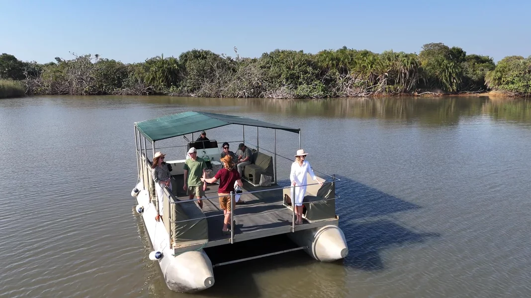 Guests line the rail of the canopied pontoon cruise boat on the flat water of the narrows, one photographing the green shoreline with a long lens.