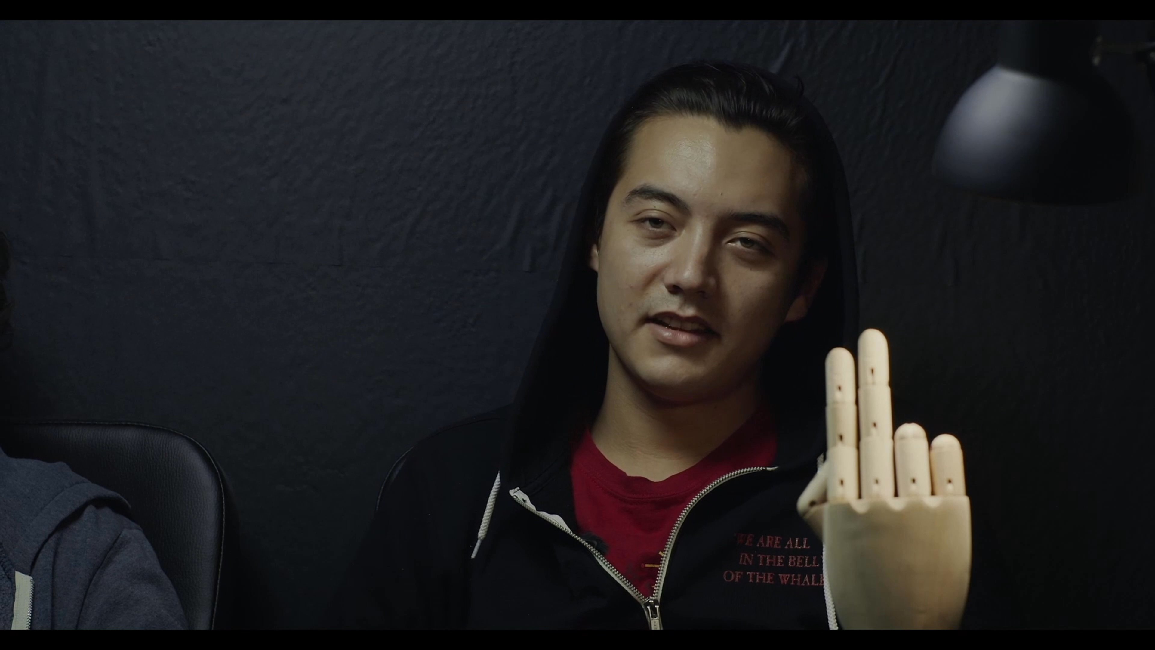 Diverse participants engage in an acting rehearsal, interacting with a wooden mannequin hand while seated in a dimly lit, professional studio setting.