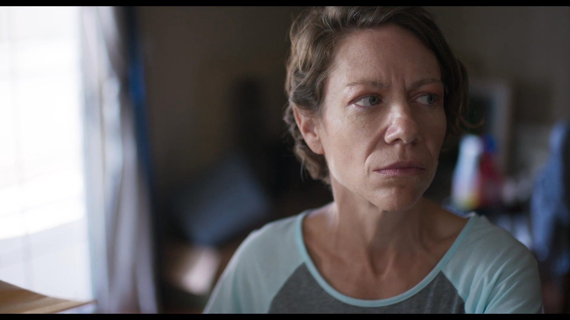 A woman experiences visible distress at a kitchen table while navigating a tense, wordless exchange that culminates in placing a wedding ring beside a glass of juice. This quiet scene captures the heavy emotional toll of a significant domestic transition.