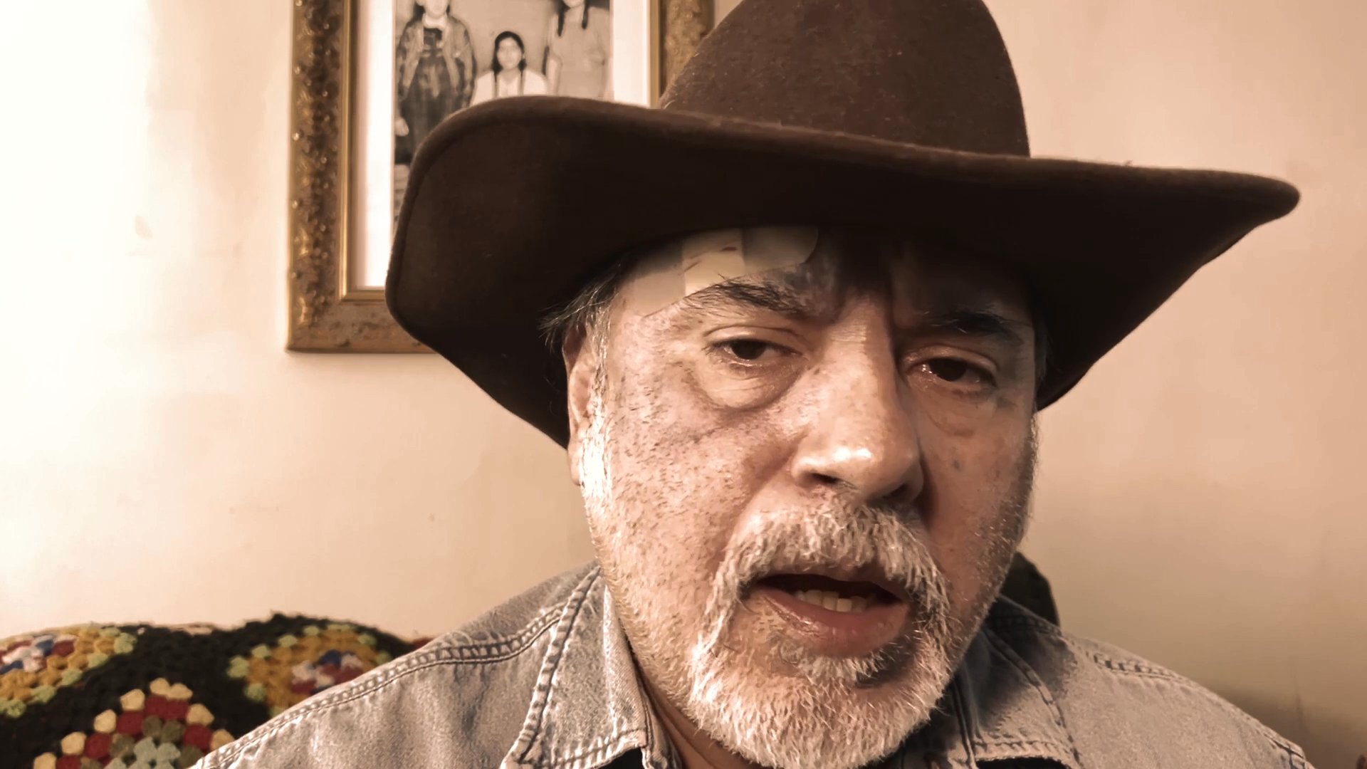 A man wearing a cowboy hat speaks directly to the camera in a pensive, storytelling manner.
