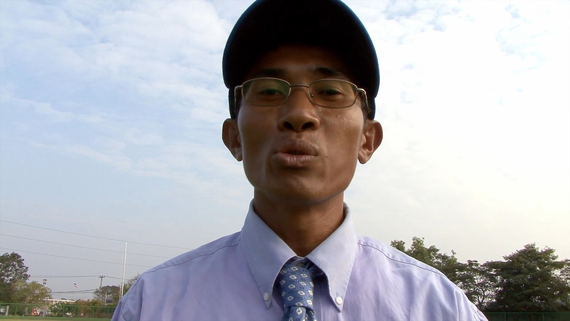 A coach discusses the Cambodian baseball team as players prepare for travel and board a bus in their uniforms.
