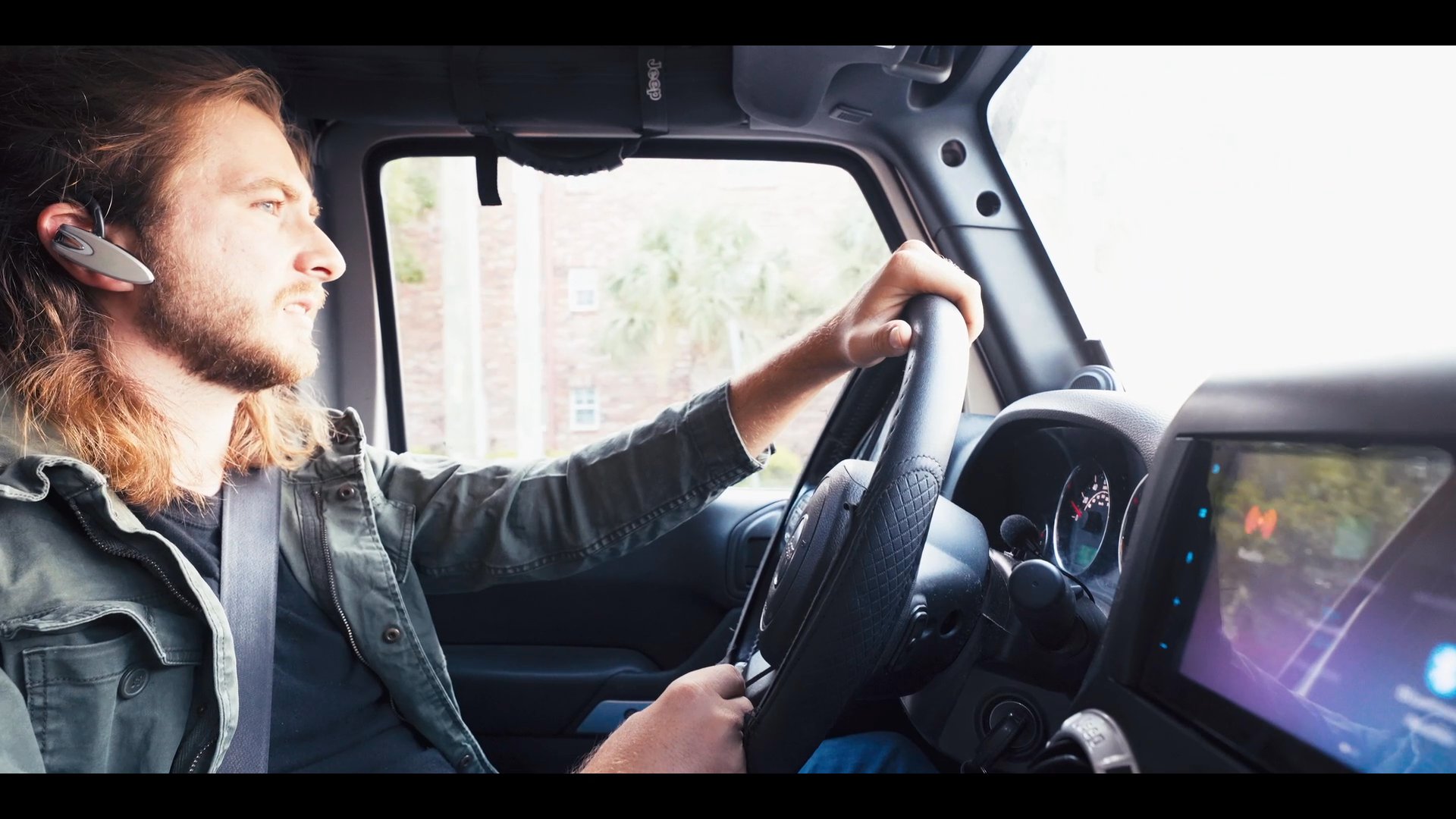 A man drives a vehicle while engaged in a professional phone conversation using a bluetooth headset. The scene transitions between his commute and an associate speaking on a phone in an outdoor setting.